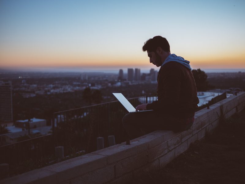 Person sitzt abends allein mit Laptop über der Stadt